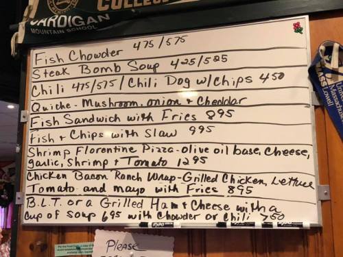 Menu board featuring various food items and prices, including chowder, sandwiches, and pizza options.