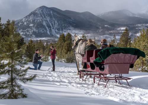A snowy landscape with a horse-drawn sleigh and people enjoying the winter scenery in the mountains.