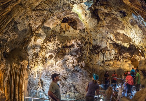 Visitors explore a cavern with impressive rock formations and lighting, showcasing stalactites and stalagmites.