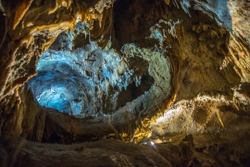 A stunning cave interior with illuminated stalactites and stalagmites, showcasing intricate rock formations and blue lighting.