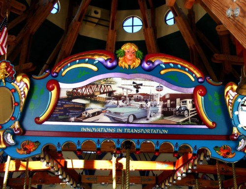 Colorful carousel top featuring a vintage transportation mural with cars and a bridge, adorned with decorative elements.