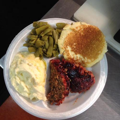 A plate with green beans, mashed potatoes, cornbread, and meatloaf with a glaze.