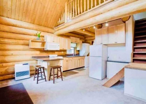 Cozy log cabin kitchen with wooden cabinets, a dining table, and stairs leading to an upper level.