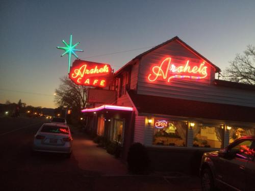 Neon-lit sign of Arshels Cafe at dusk, featuring a star decoration and an "Open" sign. Cars parked outside.