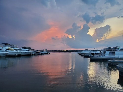 A serene marina at sunset, with boats docked and colorful clouds reflecting on the water.