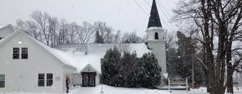 A snowy scene featuring a white church with a tall spire, surrounded by trees and a blanket of snow.