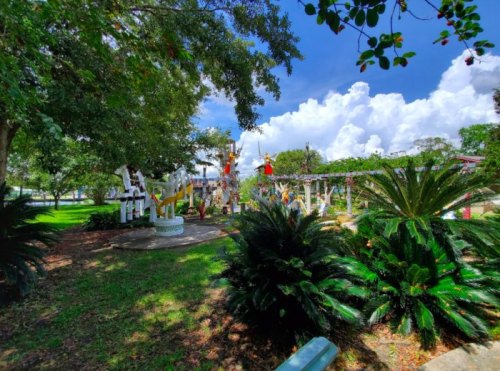 A vibrant park scene featuring colorful sculptures surrounded by lush greenery and a bright blue sky with clouds.