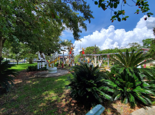 A vibrant park scene with colorful sculptures, lush greenery, and a bright blue sky with fluffy clouds.