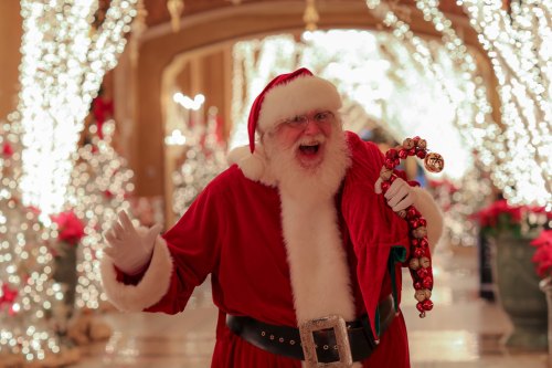 A joyful Santa Claus in a festive setting, surrounded by twinkling lights and holiday decorations, holding a candy cane.