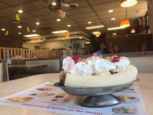 A banana split topped with whipped cream, cherries, and flags, set on a table in a cozy diner.