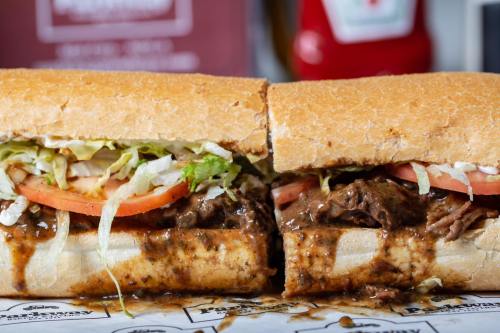 A close-up of a sandwich filled with shredded beef, lettuce, and tomato, drizzled with sauce, on a toasted hoagie roll.