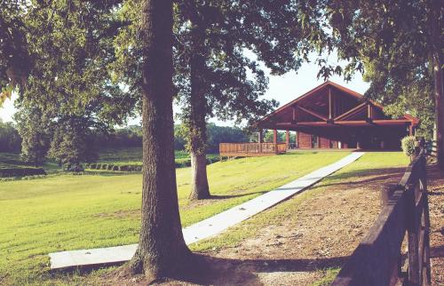 A rustic pavilion surrounded by trees and a grassy area, with a pathway leading up to it.