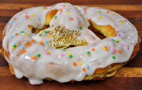 A glazed pastry topped with colorful sprinkles and a "Happy New Year" decoration on a wooden surface.