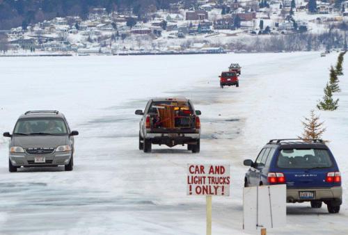 Vehicles driving on a snowy lake with a sign that reads "CAR AND LIGHT TRUCKS ONLY!" in the foreground.