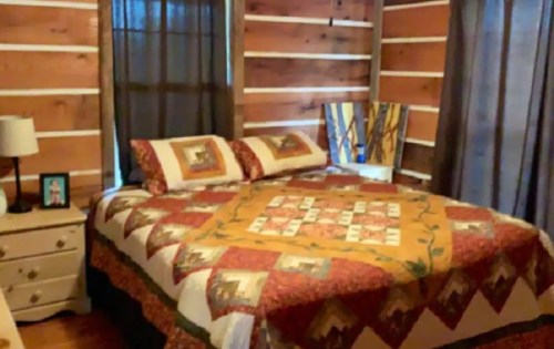 Cozy bedroom with a wooden wall, a quilted bedspread, and a bedside table with a lamp and photo.
