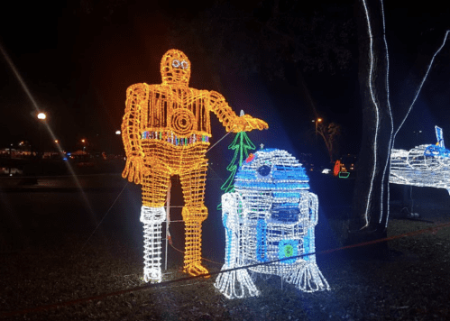 Colorful holiday lights depict two robot figures, one orange and one blue, in a festive nighttime setting.