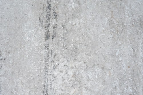 Close-up of a textured gray surface with subtle variations and markings, resembling concrete or stone.