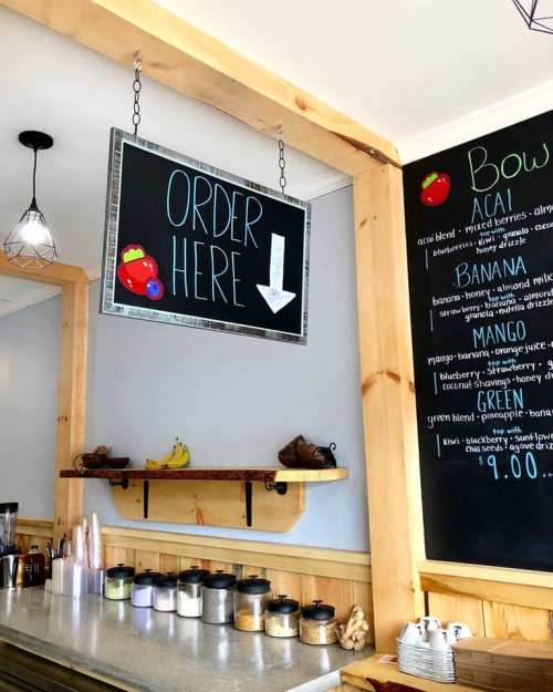 A cozy café interior with a chalkboard sign saying "Order Here" and a menu featuring smoothie bowl options.
