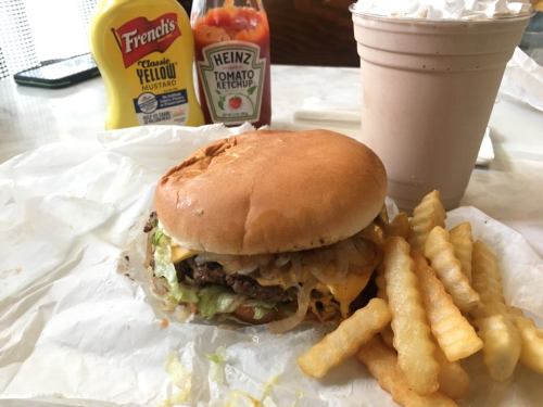 A cheeseburger with lettuce, onions, and cheese, served with fries and condiments on a table.