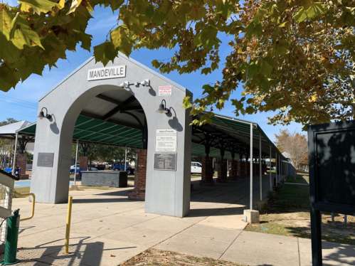 A covered pavilion with an archway labeled "Mandeville," surrounded by trees and a clear blue sky.