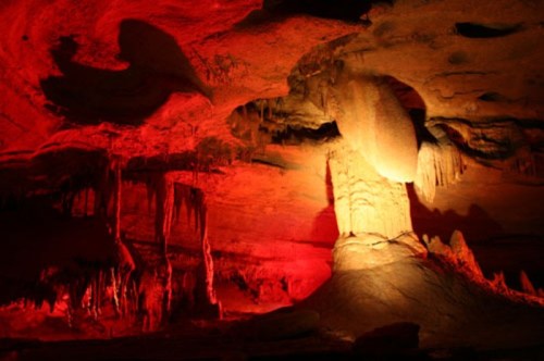 A dramatic cave interior illuminated in red, featuring stalactites and a prominent rock formation.