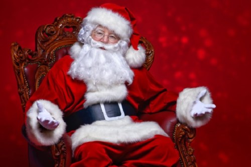 Santa Claus in a red suit and hat, sitting on an ornate chair against a festive red background.