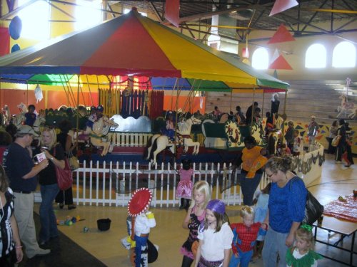 A colorful carousel surrounded by children and adults in a festive indoor setting, with decorations and costumes.