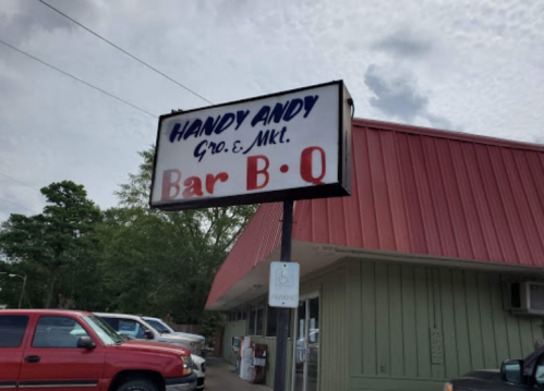 Sign for Handy Andy Grocery Market and Bar B Q, with a red roof and parked cars in the foreground.