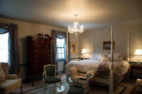 Cozy bedroom with a four-poster bed, elegant chandelier, and vintage furniture, softly lit by table lamps.