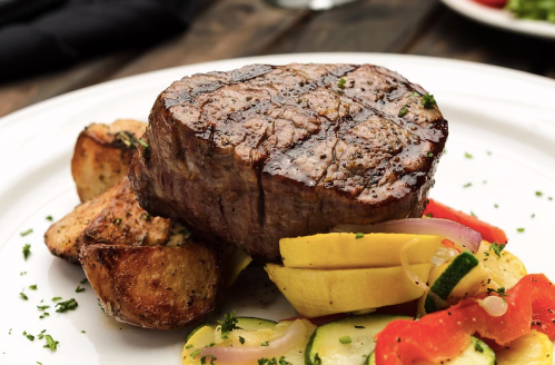 A perfectly cooked steak on a plate, accompanied by roasted potatoes and colorful sautéed vegetables.