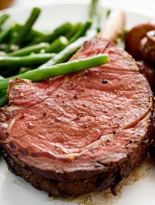 A juicy, cooked ribeye steak served with green beans on a white plate.