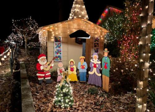 A festive scene with a decorated house, illuminated by colorful lights, featuring Santa and carolers in front.