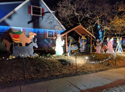 A festive outdoor scene featuring a nativity display with lights, animals, and figures in front of a decorated house.