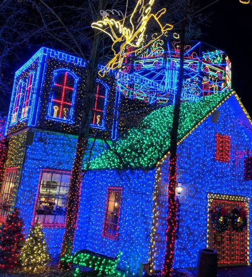 A brightly lit house covered in colorful Christmas lights, featuring a large illuminated decoration on the roof.