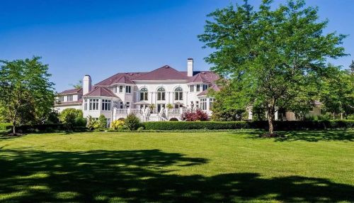 A large, elegant mansion surrounded by lush greenery and trees under a clear blue sky.
