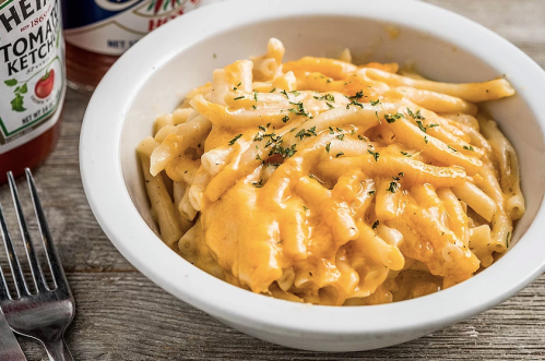 A bowl of creamy macaroni and cheese topped with melted cheese, garnished with herbs, on a wooden table.