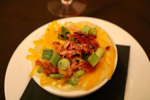 A bowl of creamy mashed potatoes topped with cheddar cheese, green onions, and crispy bacon bits.