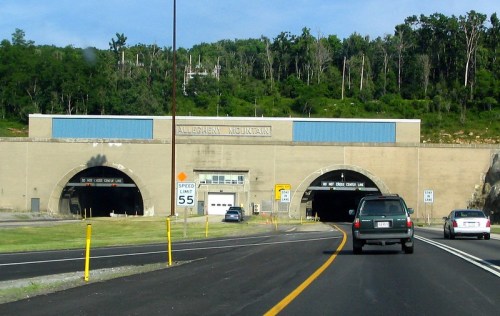 Entrance to the Allegheny Mountain tunnel, with vehicles approaching and greenery in the background. Speed limit sign visible.