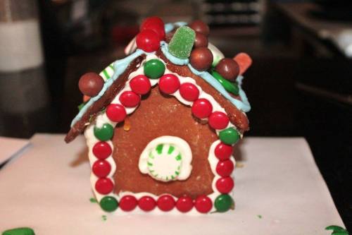 A decorated gingerbread house with colorful candies, including red and green M&Ms, gumdrops, and icing details.