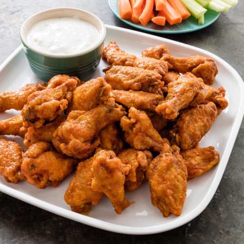 A platter of crispy chicken wings with a side of ranch dressing and fresh carrot and celery sticks.