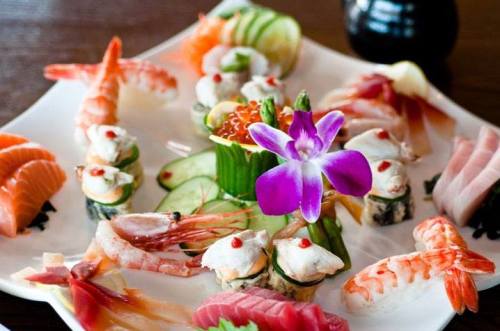 A beautifully arranged sushi platter featuring various sushi types, shrimp, and a purple flower garnish.