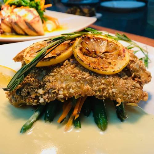 A beautifully plated dish featuring crispy fried fish topped with lemon slices, served on a bed of green beans and carrots.