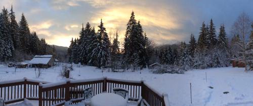 A snowy landscape with evergreen trees, a wooden deck, and a sunset sky in the background.