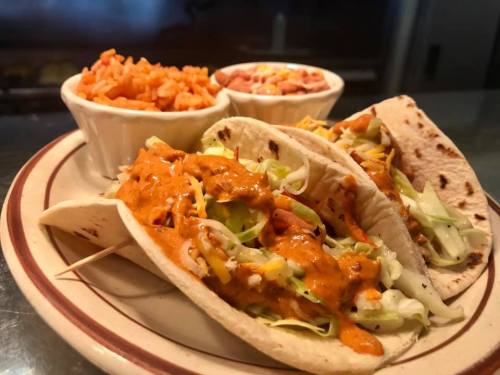 Two tacos filled with lettuce and sauce, served with rice and beans on the side.