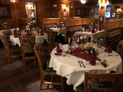 Cozy restaurant interior with wooden walls, neatly set tables, white tablecloths, and elegant decor.