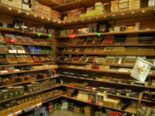 A well-stocked display of various cigar boxes and brands on wooden shelves in a shop.