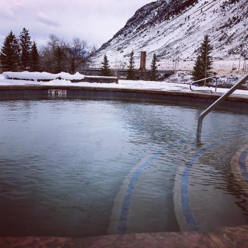 A hot tub surrounded by snow-covered trees and mountains, with steam rising in a serene winter landscape.