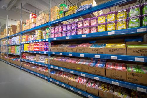 A colorful candy aisle with shelves stacked high with various candy boxes and bags in a warehouse setting.