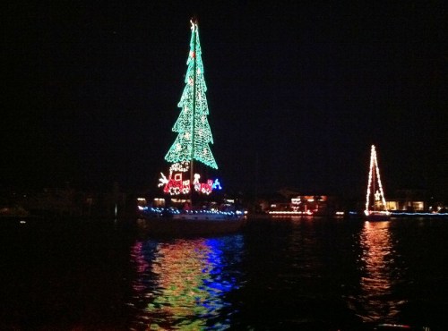 A brightly lit Christmas tree boat adorned with colorful lights, reflecting on the water at night.
