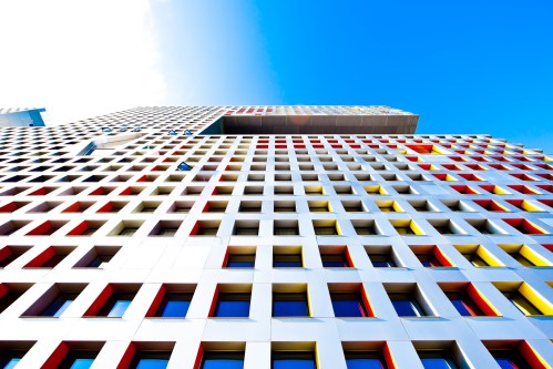 A modern building with a colorful grid pattern of red, yellow, and white windows against a bright blue sky.